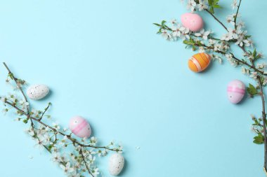 Düz paskalya yumurtaları ve çiçekler mavi arka planda.