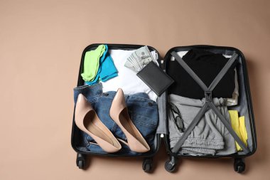 Gri masadaki renkli bavulun yanında farklı kıyafetler ve aksesuarlarla dolu bavul. Metin için boşluk