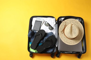 Sarı arka planda ayakkabı ve şapkalı bavul.