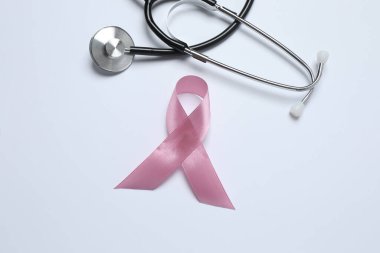 Göğüs kanseri farkındalığı ayı. Beyaz arka planda pembe steteskop ve pembe kurdele. Yakın plan.
