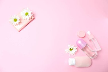 Kozmetik şişesi ve pembe arka planda çiçekler olan boş beyaz kağıt. en üstteki görünüm.