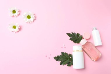 Kozmetik şişeli kompozisyon ve pembe arka planda çiçekler, üst görünüm