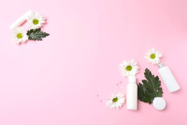Beyaz kozmetik şişeleri ve pembe arka planda çiçekleri olan düz bir kompozisyon. Metin için boşluk