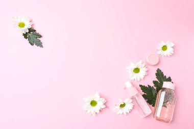 Renkli arka planda bir şişe kozmetik, çiçek ve papatya çayı.