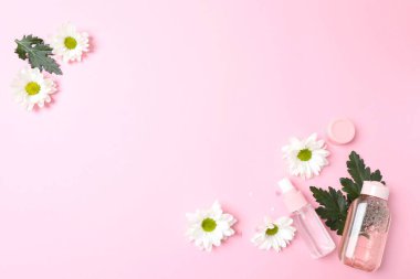 Pembe çiçeklerin ve pembe arka planda kozmetik şişelerin üst görüntüsü.