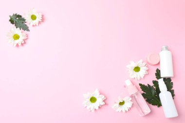 Pembe arka planda kozmetik şişeler ve çiçekler