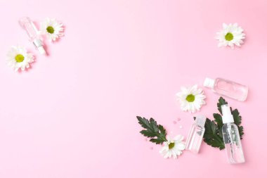 Pembe çiçekli kozmetik şişeler ve pembe arka planda yapraklar. düz alan, üst görünüm, kopyala boşluk