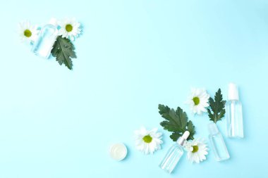 Mavi arka planda kremalı, çiçekli ve papatyalı kozmetik şişeleri, düz zemin, fotokopi alanı, güzellik, kozmetik konsept