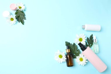 Mavi arka planda kozmetik şişe ve çiçekler. Kopyalama alanı olan düz.