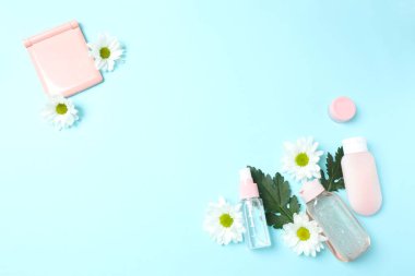 Kozmetik şişeleri ve pastel mavisi arka planda çiçekleri olan düz bir yer. düz yat