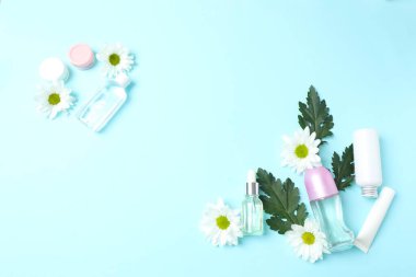 Mavi arka planda kozmetik şişeler, çiçekler ve yapraklar.