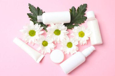 Beyaz arka planda kozmetik ürünler, krem ve çiçekler.