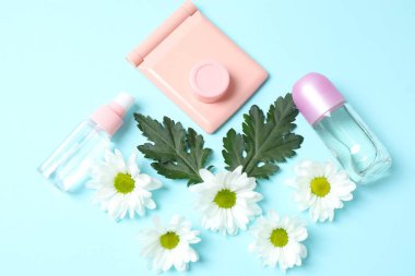 Papatya çiçekli bir şişe kozmetik kremi ve pembe arka planda renkli çiçekler.