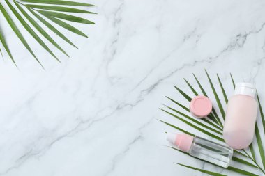 Kozmetik, güzellik ve vücut bakım ürünleri konsepti - Pembe palmiye yaprağının ve kozmetik ürünlerinin üst görünümü