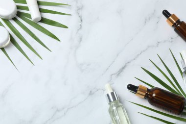 Doğal serumlu kozmetik şişeler ve mermer zemin üzerinde yaprak