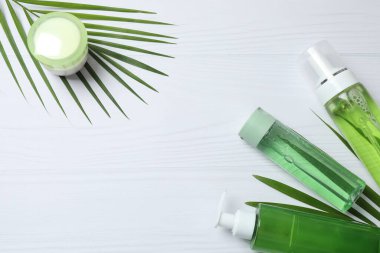 Beyaz mermer zemin üzerinde krema ve yeşil yapraklı kozmetik şişeleri, düz yatıyordu