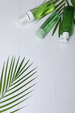 Beyaz zemin üzerinde yeşil yapraklar, şişe ve kozmetik şişeler ile düz konum