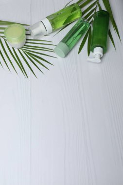Doğal kozmetik ürünleri ve beyaz ahşap arka planda yeşil yapraklı şişeler.