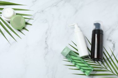 Kozmetik şişeleri ve mermer zemin üzerinde yaprakları olan düz konum