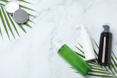 Beyaz mermer arka planda kozmetik ürünler, bir şişe su, havlu ve okaliptüs yaprakları.