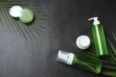 Gri arkaplanda kozmetik ürünleri ve yaprakları içeren kompozisyon