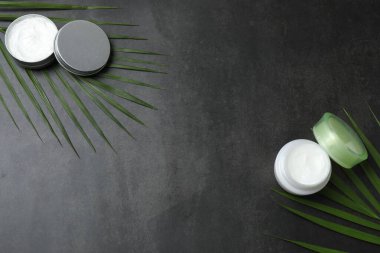 Koyu beton masa üzerinde palmiye yaprakları olan kozmetik ürünleri