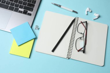 Not defteri, gözlük, dizüstü bilgisayar, kalem, not defteri, bardaklar ve mavi arka planda bir fincan kahve..