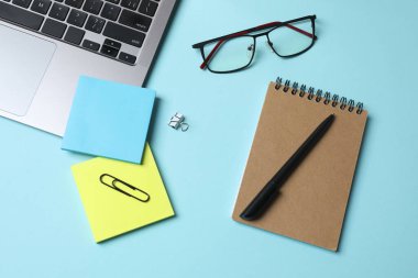 Not defteri, dizüstü bilgisayar, gözlük, kalem, not defteri ve gözlük ile ofis çalışma alanı düz görünümü mavi arkaplanda, kopyalama alanı