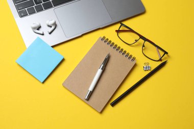 Sarı arka planda defter, gözlük, akıllı telefon, kalem ve defter ile modern iş yerinin üst görünümü