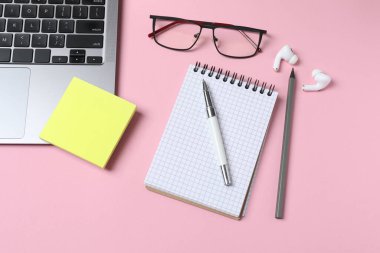 Pembe arka planda modern dizüstü bilgisayar, not defteri ve kalemle düz konum