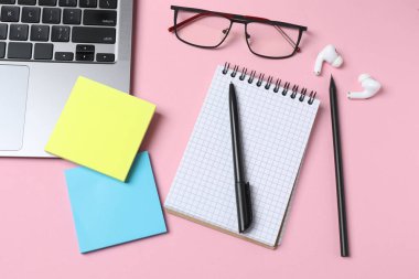 Dizüstü bilgisayarı ve pembe tahta arka planda gözlüğü olan düz bir kompozisyon. Metin için boşluk