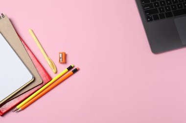 Pembe arka planda dizüstü bilgisayar, kalem ve not defteri.