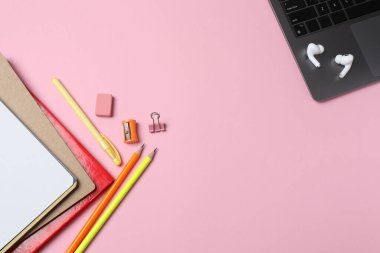 Bilgisayar, kırtasiyeli defter, kalemler, gözlükler ve pembe arka planda telefon. en üstteki görünüm.