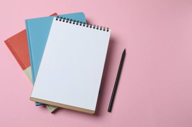 Boş kağıt, pembe arka planda defter ve kalem. Dizaynınız için kopyalama alanı olan en üstteki görünüm.