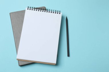Mavi zemin üzerinde kalem ve kalem bulunan boş beyaz kağıt defterin üst görünümü