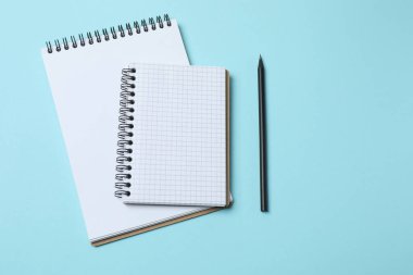Beyaz kâğıtlı not defteri, mavi kalem, kalem ve açık mavi zemin üzerinde bir defter, düz yatış, üst görünüm.