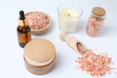 Temel yağlı doğal tuz, tahta kaşık ve beyaz arka planda bir şişe gül çiçeği, yakın plan.