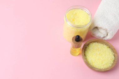 Bir kase doğal banyo tuzu, sabun ve havluyla banyo fırçası sarı arka planda, üst manzara