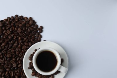 Beyaz arka planda kahve ile beyaz fincanda siyah kahve çekirdekleri..