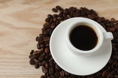 Beyaz fincan tabağı ve kahve çekirdekleri olan ahşap bir masada bir kupa kahve.