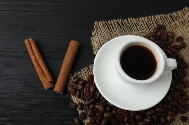 Kahve fincanı, tarçın çubukları ve kahve çekirdekleri. Siyah ahşap arka planda. en üstteki görünüm.