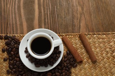 Bir fincan kahve, tarçın ve tahtadan arka planda kahve taneleri..