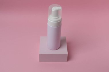 Pembe arka planda bir şişe makyaj kremi ve yüz maskesi.