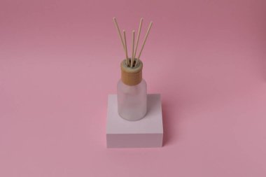 Pembe arka planda tahta çubukla beyaz ve pembe bir mumun dikey görüntüsü.