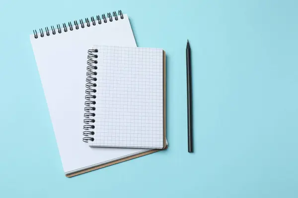 Beyaz kâğıtlı not defteri, mavi kalem, kalem ve açık mavi zemin üzerinde bir defter, düz yatış, üst görünüm.