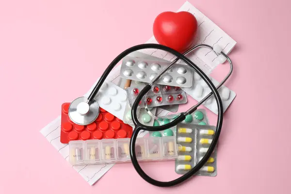 Tıbbi steteskop ve pembe arka planda haplar. en üstteki görünüm