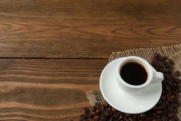 Kahve fincanı ve kavrulmuş kahve çekirdekleri eski ahşap masada.
