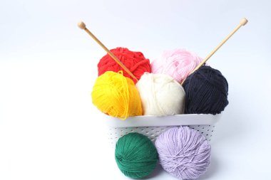 Gri bir arka planda beyaz bir sepette renkli iplik topları.