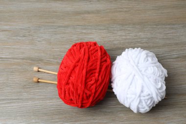 Ahşap masada kırmızı iplik ve örgü iğneleri.