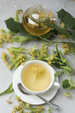 Ahşap zemin üzerinde ıhlamur çiçekleri olan bir fincan bitki çayı.